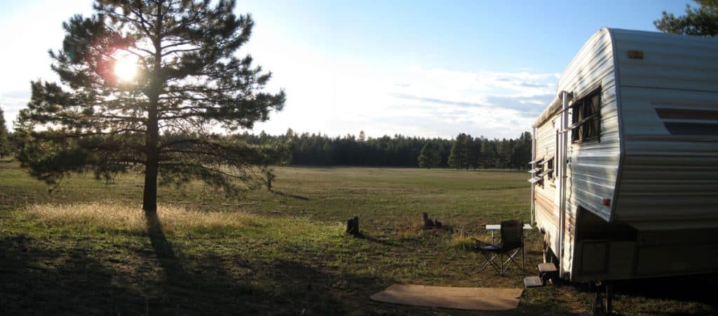 5th wheel travel trailer camped at meadow's edge as sun dips behind a pine tree